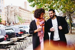 Smiling man and woman having a conversation while holding drinks and walking outside.